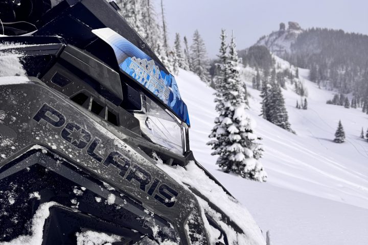 Snowmobile in snowy landscape with trees and distant mountain.